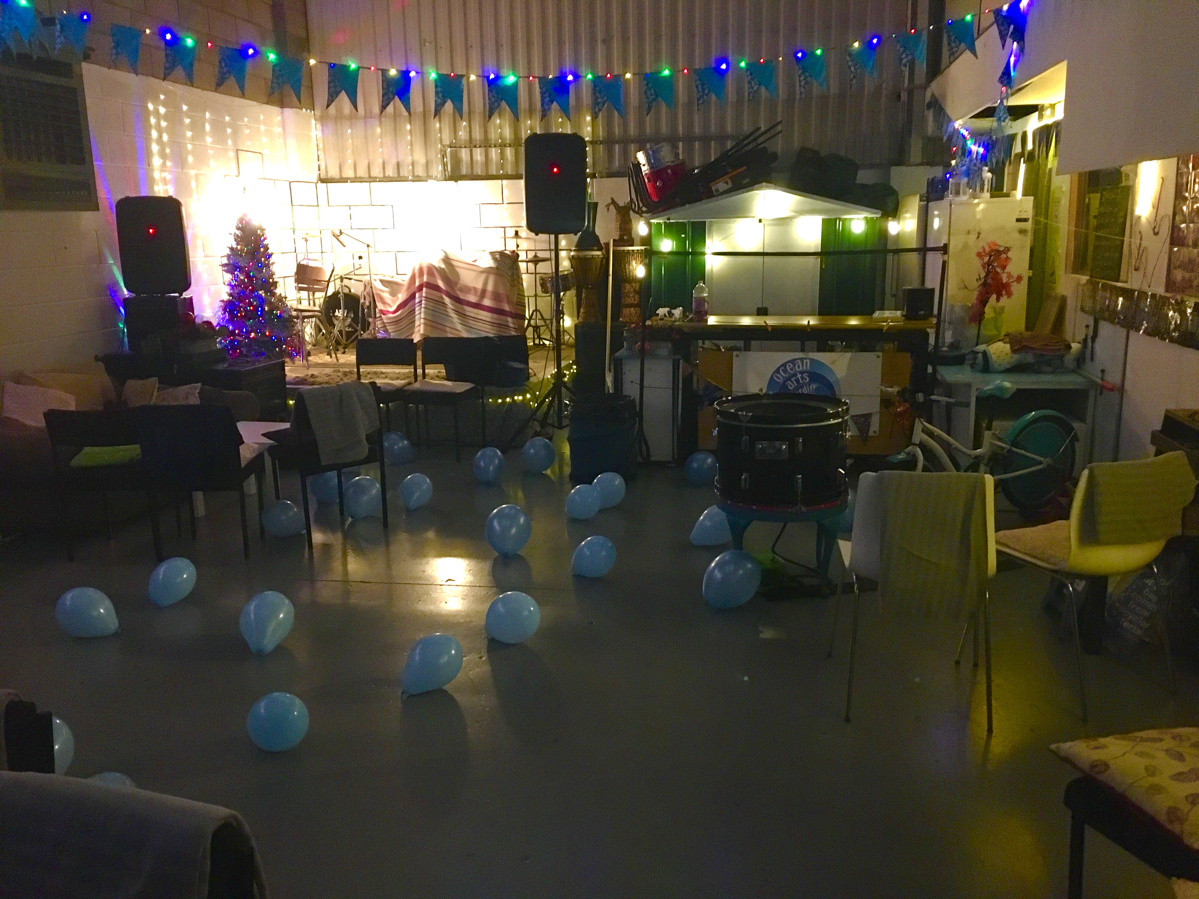 This is the main space in Ocean Arts Cardiff set up for a birthday party.  There is a small stage, sound system, lots of fairy lights and blue balloons on the floor.  