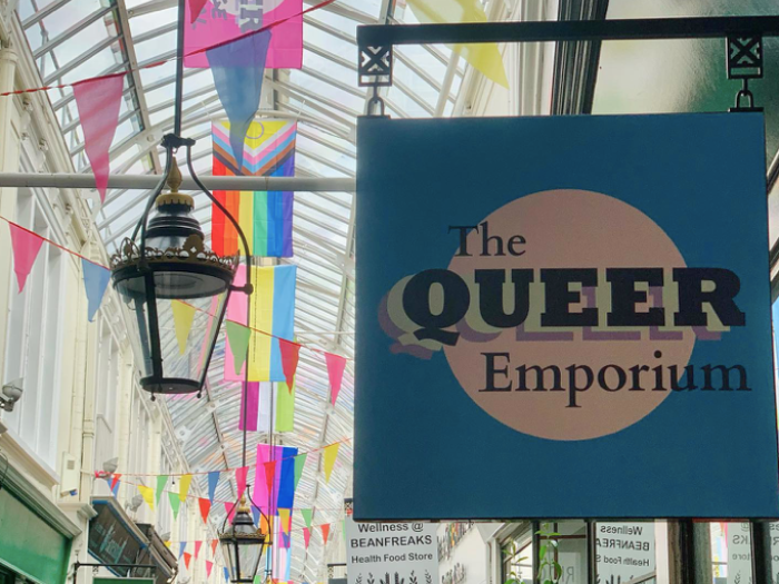 A sign of The Queer Emporium logo outside of their store, looking onto the arcade.