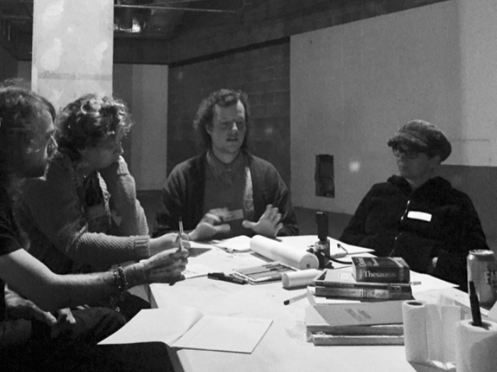 The image features members of the Lone Worlds collective sitting around a table in a meeting