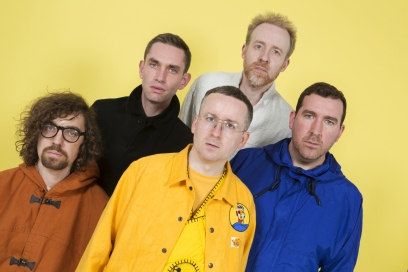 Five members of Hot Chip leaning to right against yellow backdrop 
