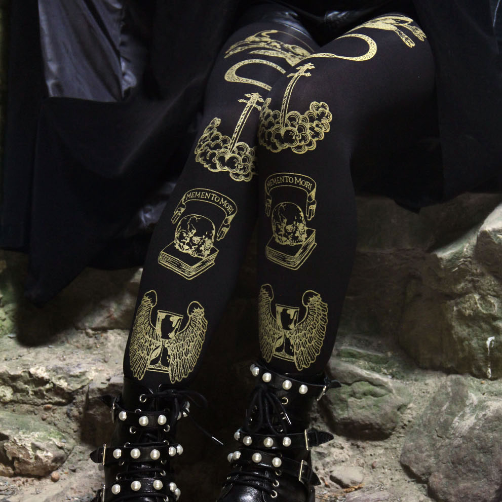 Screen printed tights with a design of skulls, winged hour-glasses, snakes and the phrase "Memento Mori" printed in gold on black tights. The background is of dimly lit stairs in a castle.
