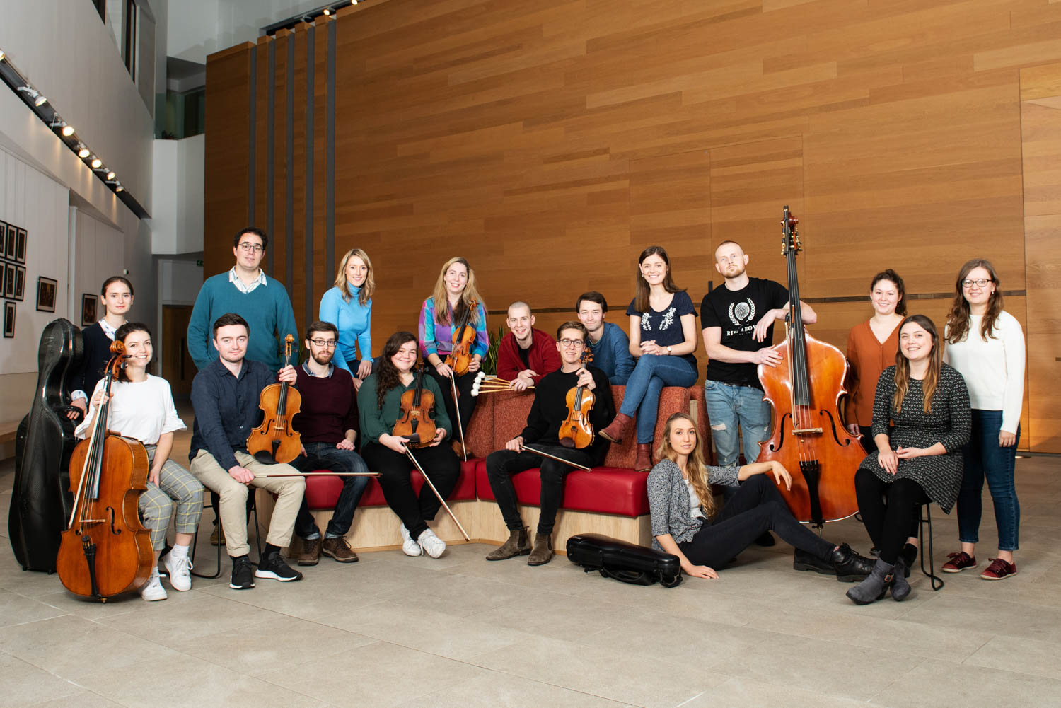 A group of musicians standing and sitting holding string instruments, smiling at the camera