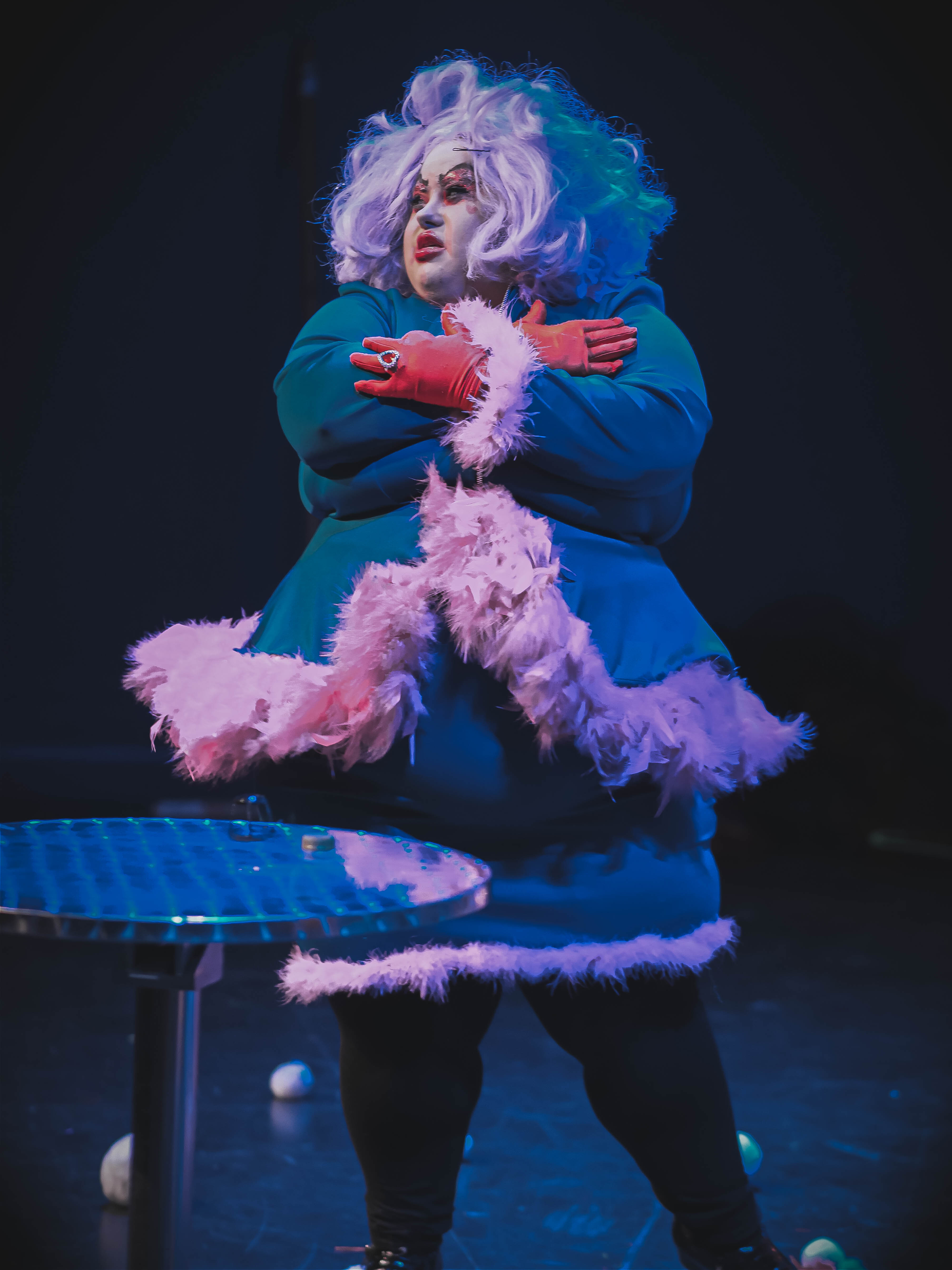 Miss Shade, drag queen from House of Deviant wearing a teal coloured peplum suit with pink feathers and a lilac wig.