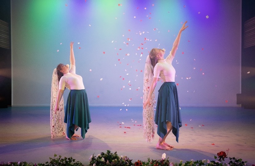Two dancers in costume with petals coming down from the ceiling