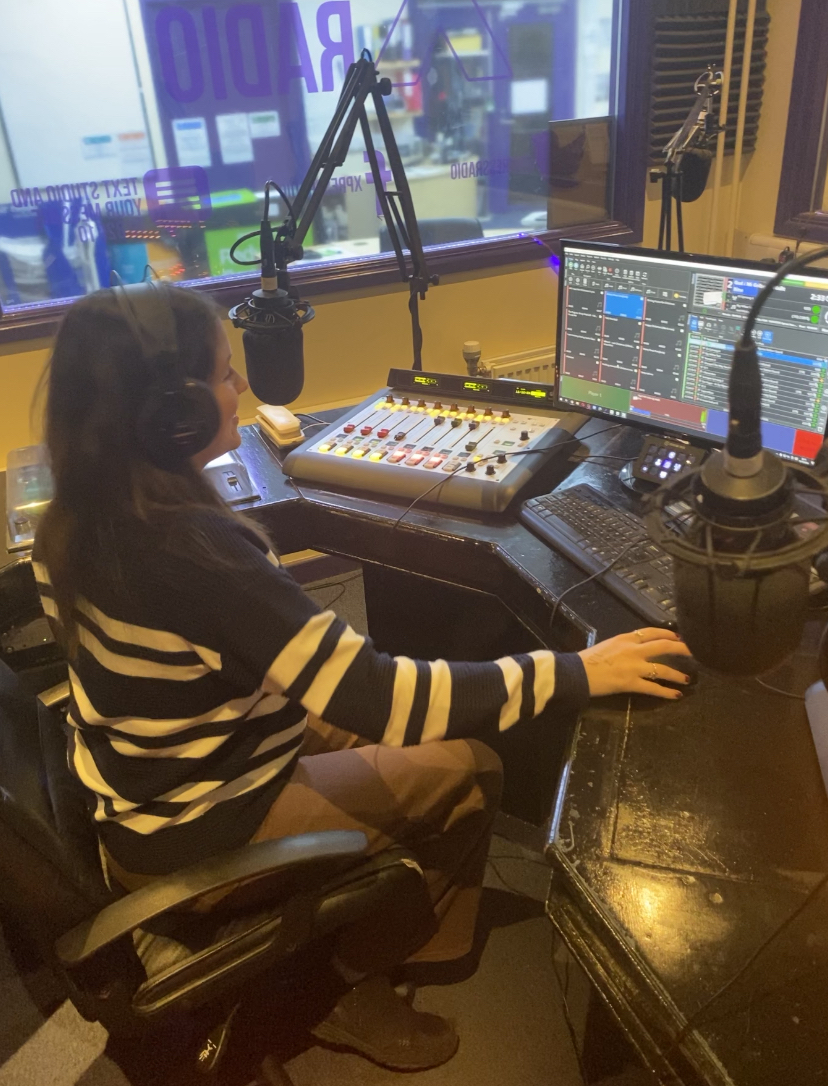 Jess sitting in a podcast booth with equipment in front of her