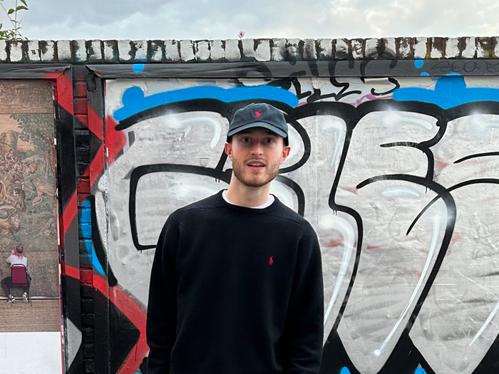 A person wearing a cap standing in front of a wall with graffiti