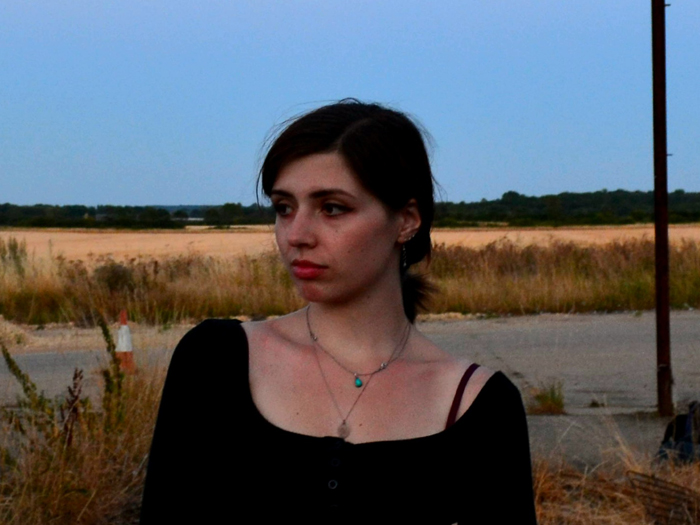 A person with dark hair wearing a black shirt with a landscape in the backgroun