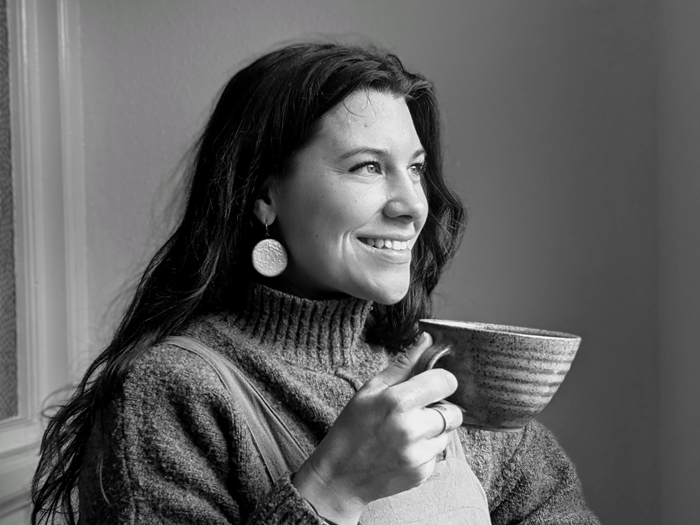 A black and white photo of a person with long hair holding a ceramic cup.