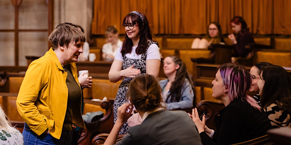 people talk in a circle, a lady wears a yellow coat with her hands in her pocket talking to students