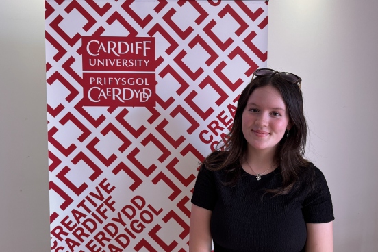 Jess stands in front of the Creative Cardiff banner wearing a black top