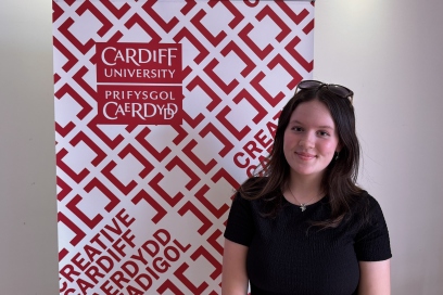Jess stands in front of the Creative Cardiff banner wearing a black top