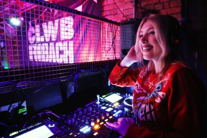 DJ Katie Owen smiling in front of a set of decks at Clwb Ifor Bach.