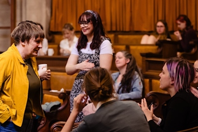 people talk in a circle, a lady wears a yellow coat with her hands in her pocket talking to students
