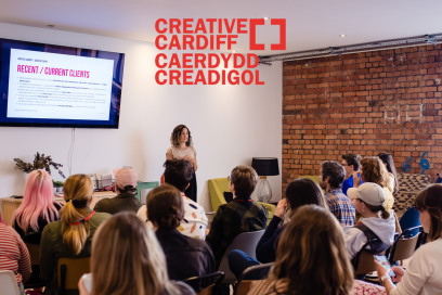 Creative Cardiff logo on an image of a woman presenting to a room of people